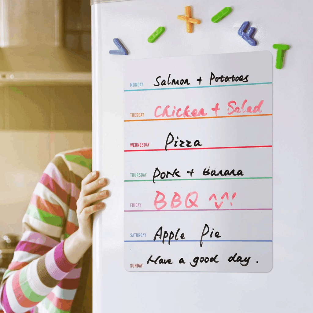  A list of the days of the week for meal planning, each in a different bright color.  Next to each day is written in dry erase marker, a meal idea. This is hung on a white refrigerator with brightly colored children's letter magnets above it.  A hand is seen opening the fridge door. 