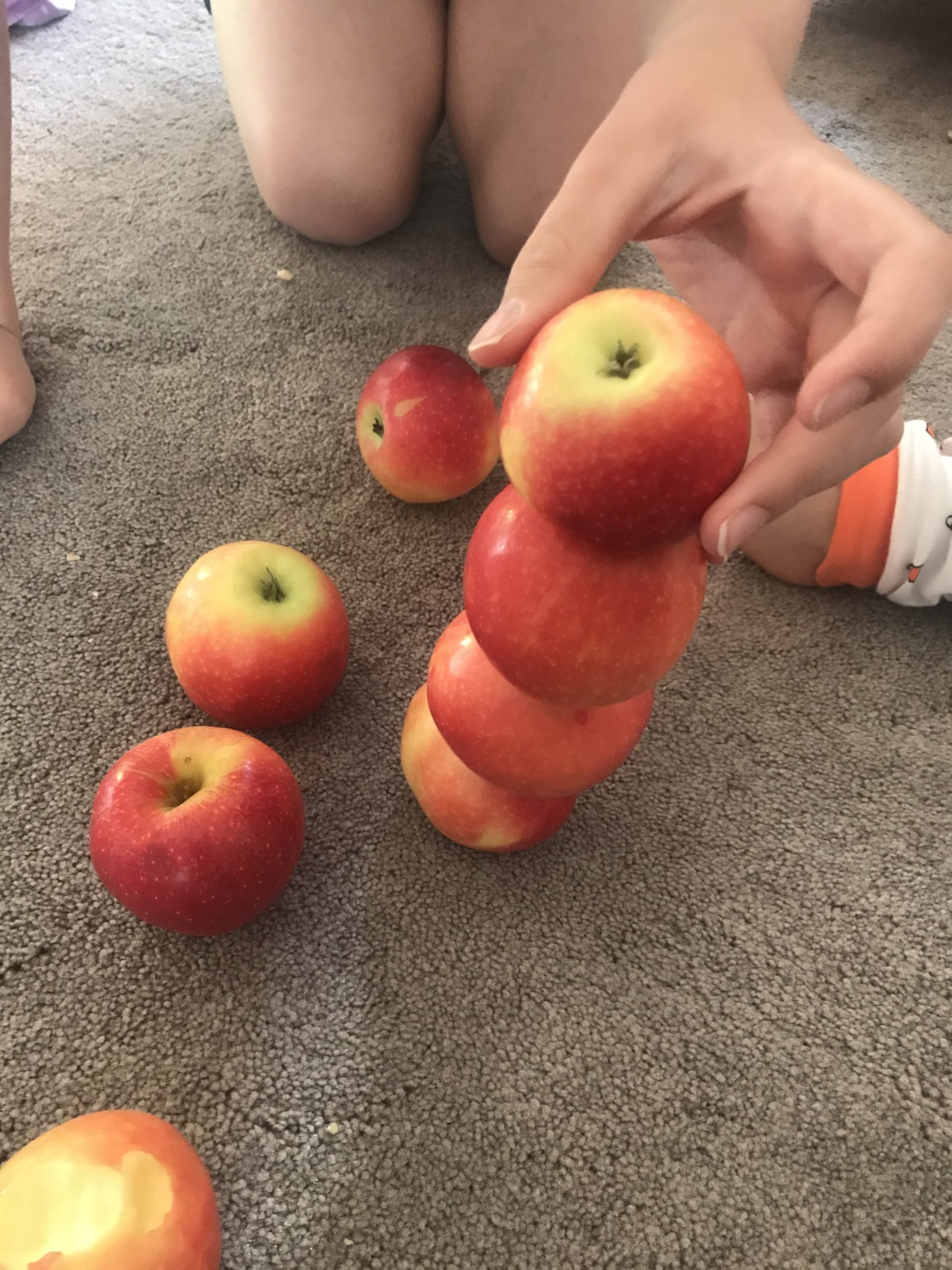 A child is stacking up apples as high as they can. 