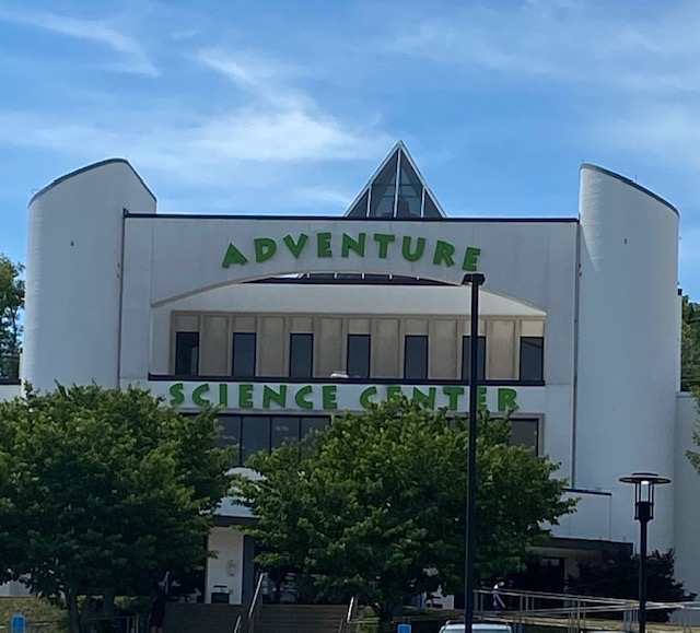 Photo of the outside of the Adventure Science Center in Nashville, TN. Buildins is white with bright green letters depicting it's name.