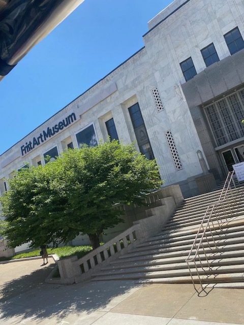 Picture of a large white building. A large wide staircase leads up to doors. Large black letters say, "Frist Art Museum". There is a wide but short green tree in front of the building.