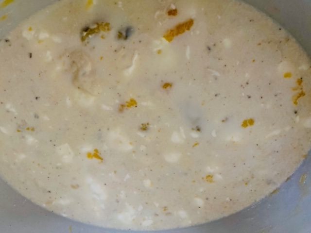 A cream colored soup with white spots and darker spots in a white bowl.