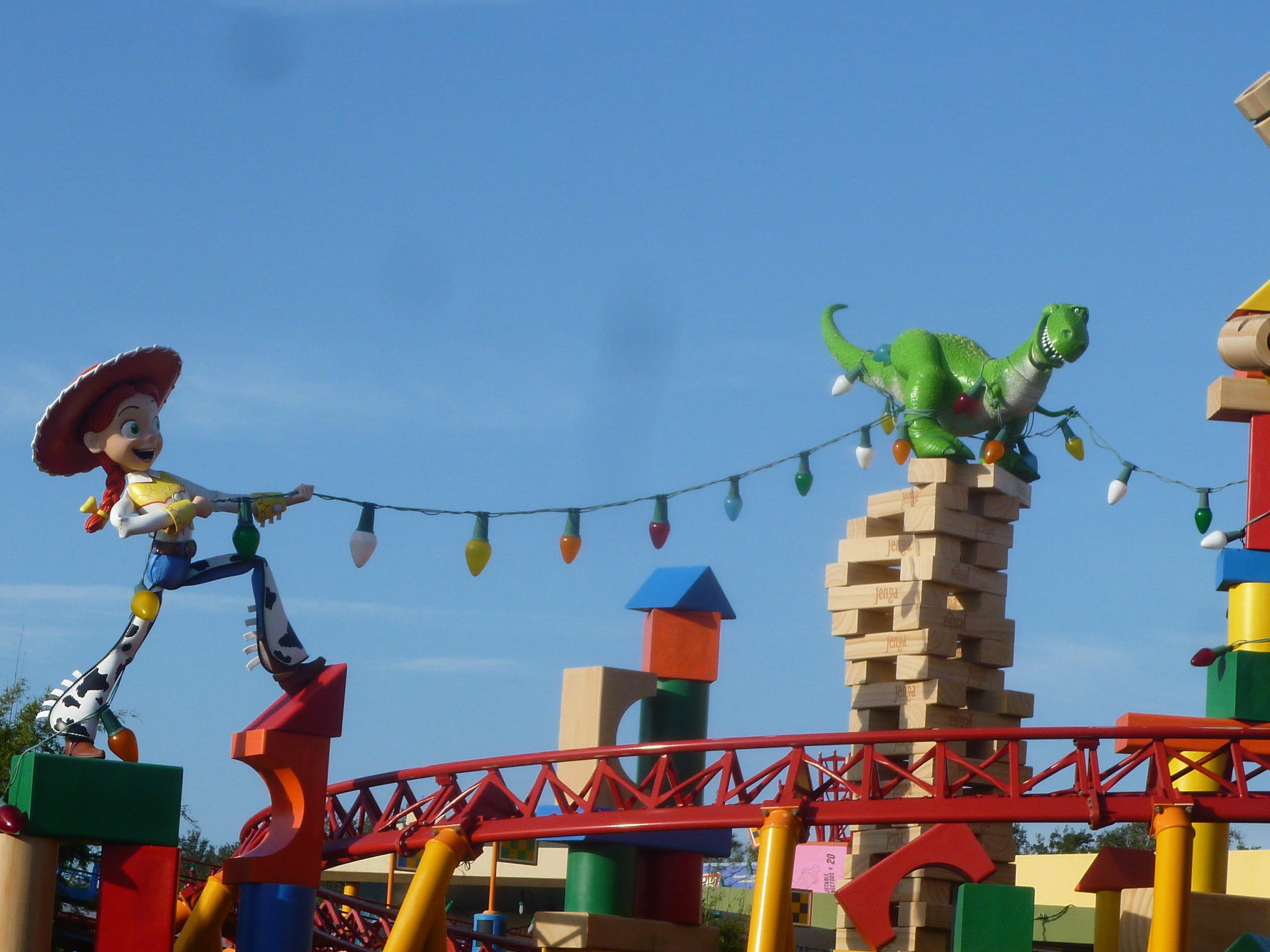 Photo of Toy Story Land in Hollywood Studios Disney World.  A giant Jessie from the movie Toy Story, along with Rex the dinosaur string Christmas lights in "Andy's backyard" amongst giagantic toy blocks, car track (which is also a roller coaster track) and Jenga blocks. 
