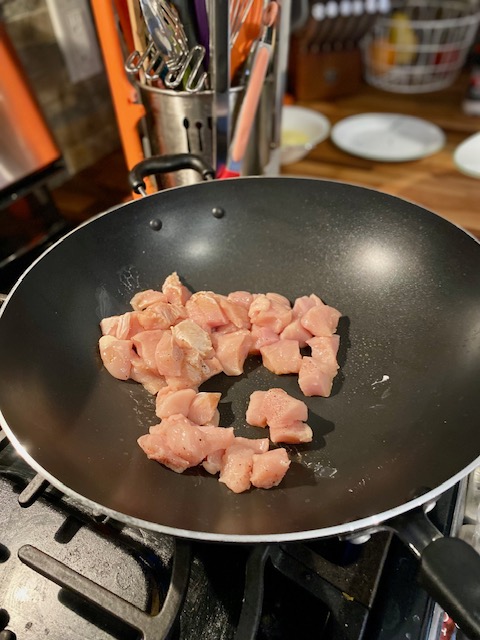 Raw, one inch cubes, of chicken in a wok.