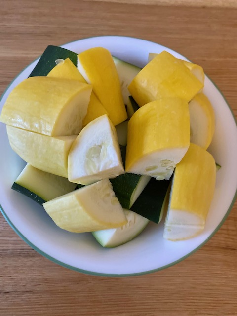 A white bowl full of chopped yellow squash and zucchini. The vegetables are chopped into 2 inch pieces.