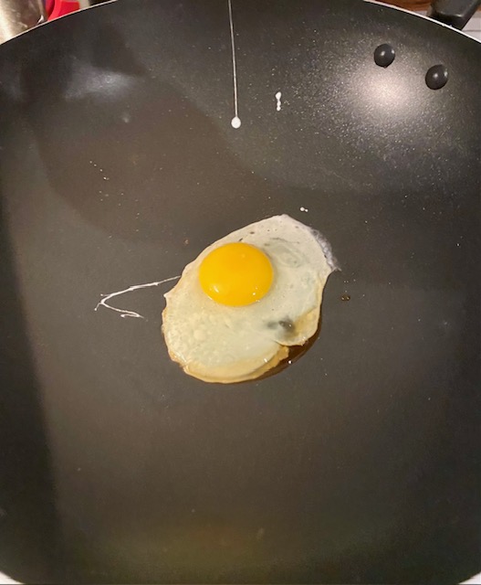 One fried egg in a black wok.
