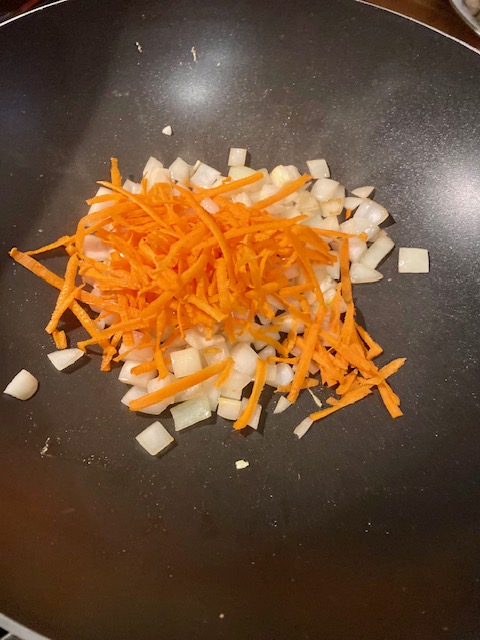 Chopped white onion with shredded carrot on top. Cooking in a black wok.