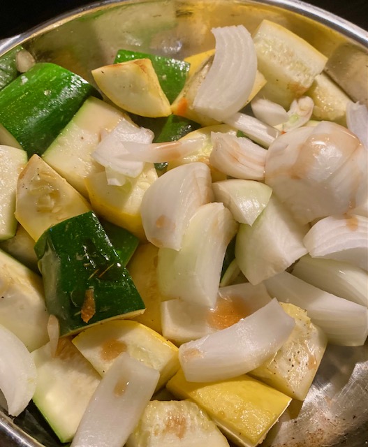 Chopped pieces of yellow squash, zucchini and slices of white onion cook in a silver frying pan.