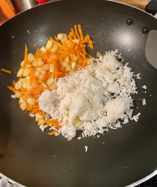 On the right side of a black wok is a mixture of shredded carrot and small pieces of white onion.  On the left is white rice. 