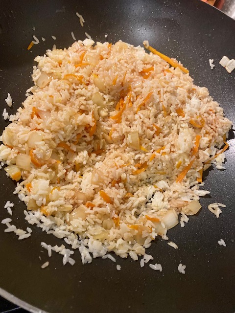 Rice, chopped white onion and shredded carrot cook in a black wok.