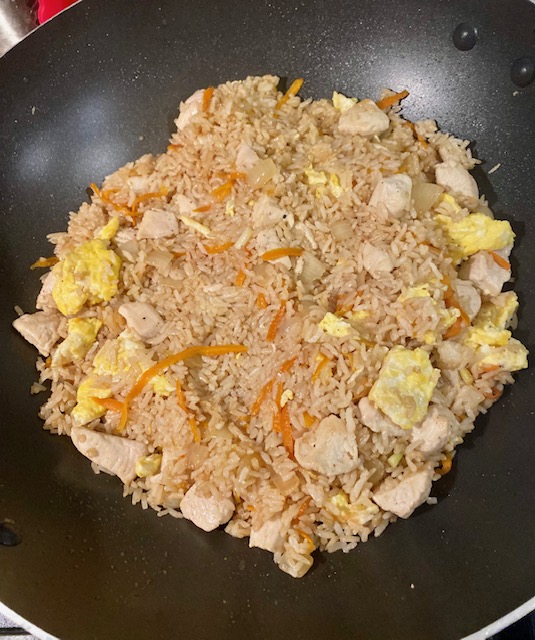 Fried rice, small pieces of scrambled egg, one inch cubes of cooked chicken, chopped white onion and shredded carrot are in a black wok.