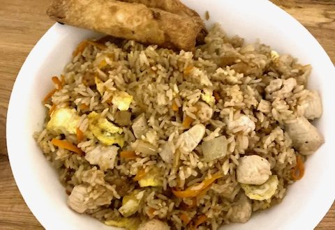 A white bowl holds chicken fried rice. Two egg rolls are placed towards the top of the bowl.
