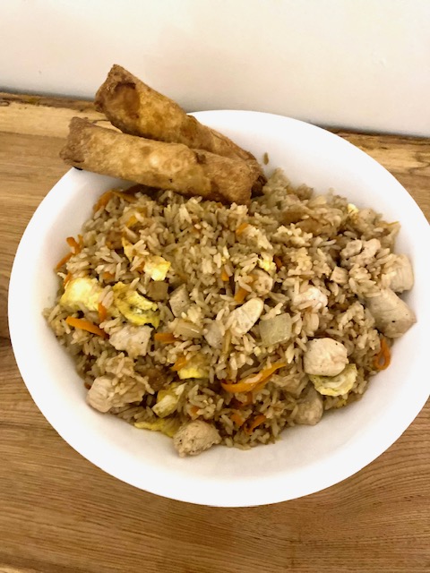 A white bowl holds chicken fried rice. Two egg rolls are placed towards the top of the bowl.
