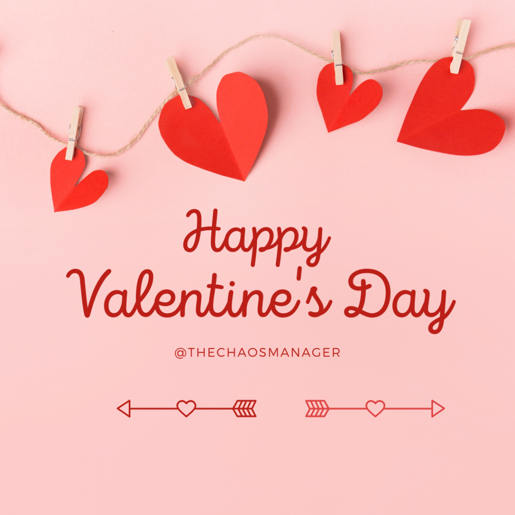 A pink background with red lettering.  The lettering reads, "Happy Valentine's Day" in a cursive font.  Underneath in block letters it says "@TheChaosManager.  There is a  garland of red paper hearts across the top.  They are hung on a clothesline.  