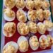Over a dozen deviled eggs sit on a tray. The tray has a red bottom outlined with a white stripe. The rim of the tray is holiday green. Each deviled egg is filled with yellow filling and topped with red sprinkles of paprika.