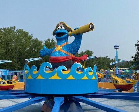 At Sesame Place theme park, a large statue of Cookie Monster is dressed with a pirate hat and holds a spy glass.  He is in the center of a theme park ride.  The small pirate ships hold park guests as they spin around the Cookie Monster statue.  