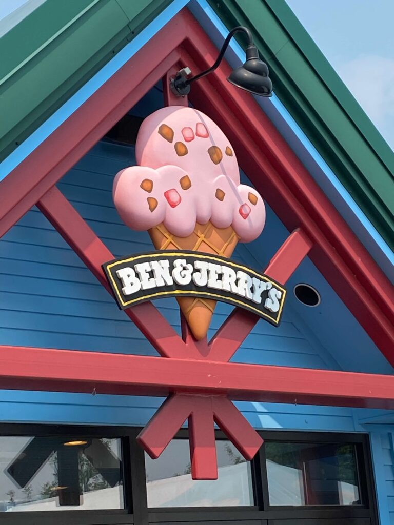 The exterior of the Ben & Jerry's Factory.   A large pink ice cream cone with the Ben & Jerry's logo hangs on the front of the building. 