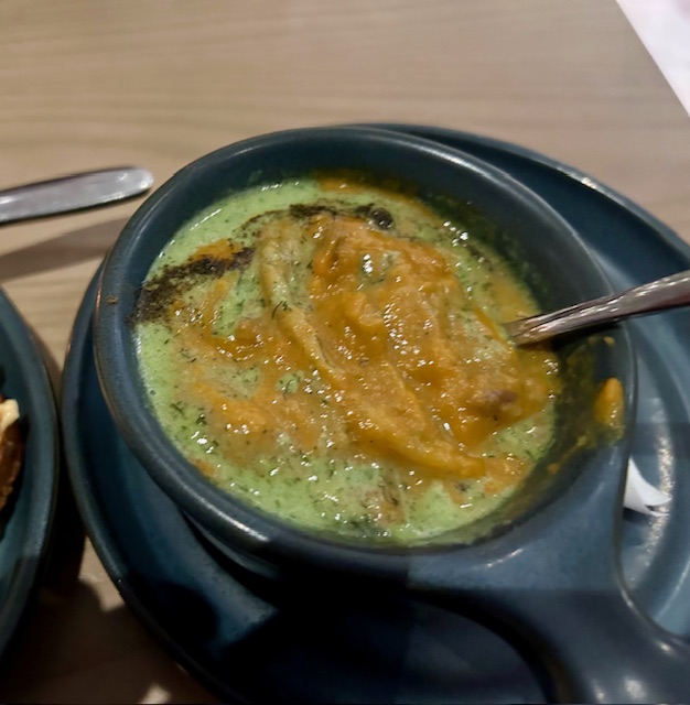 A black crock of soup sits on a small black plate at Cafe Momentum.  The light green soup has pumpkin puree on top.  