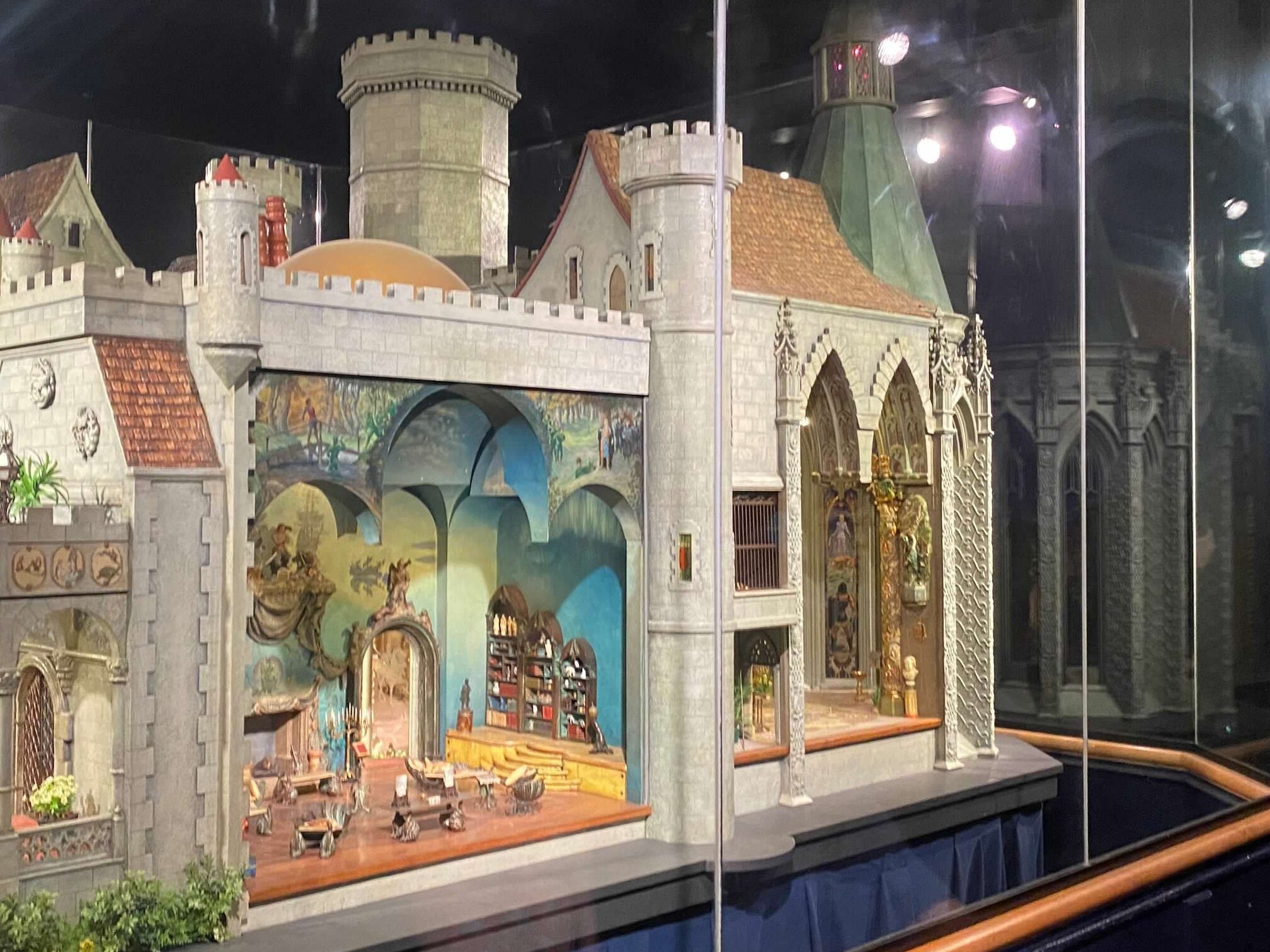 A castle themed doll house is almost 9 feet long.  It is behind glass and up on a platform on display at the Griffin Museum of Science and Industry.