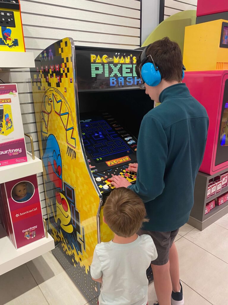 Brothers playing on a PacMan arcade machine in the American Girl store. 