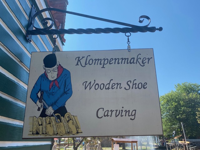 A sign at Nelis' Dutch Village has a drawing of a man in Dutch clothing carving wooden shoes. It reads, "Klompenmaker Wooden Shoe Carving".
