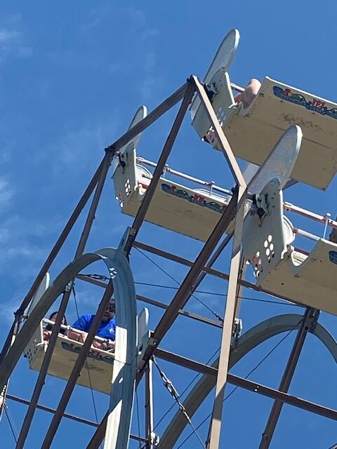 The top of a ferris wheel can be seen against a clear blue sky.