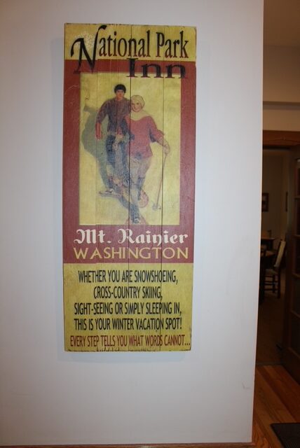 A yellow vintage sign reads: National Park Inn Mt. Rainier Washington

It features a couple on skis and boasts the mountain being a winter vacation spot. 
