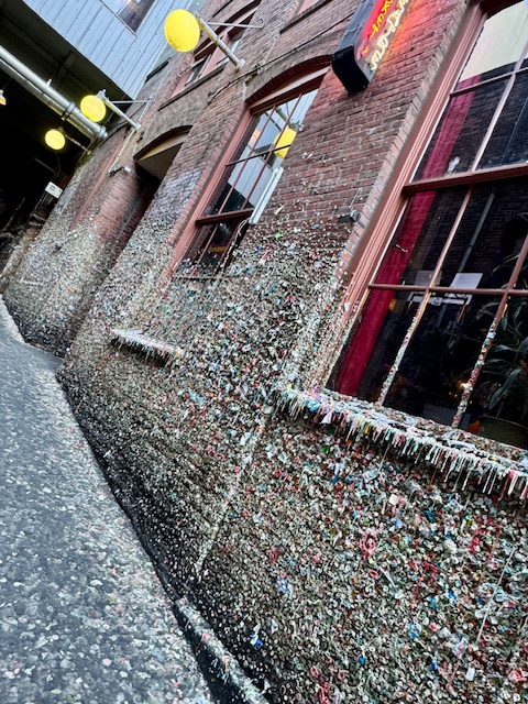 An alley of brick buildings with several large windows has its walls covered with chewed up pieces of gum. Seattle Gum Wall