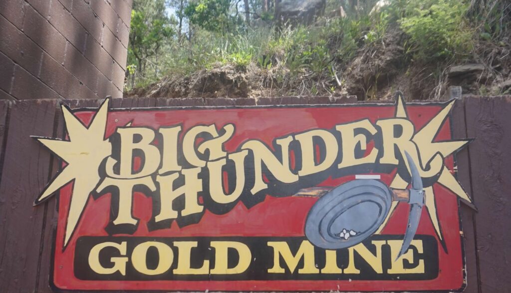 A red sign advertises, "Big Thunder Gold Mine" in large yellow block letters.  There is also a photo of a mining pan and pick axe on the sign. 