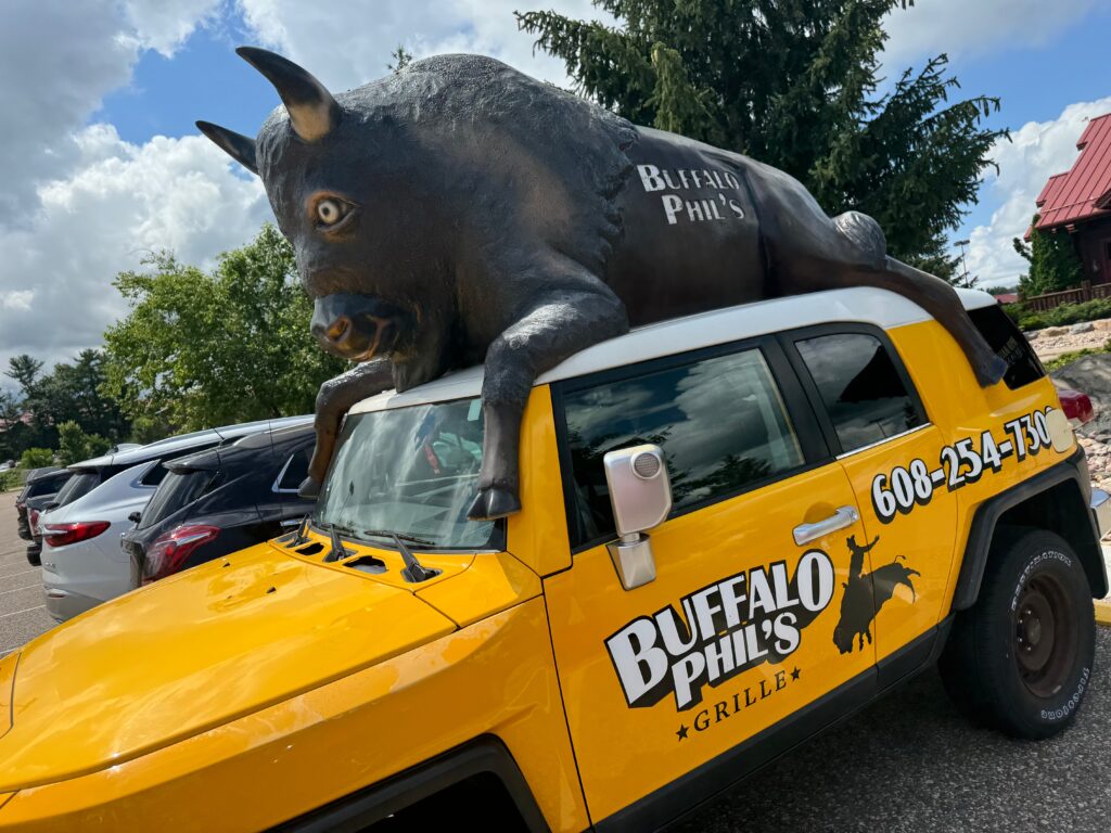 A yellow jeep says, "Buffalo Phil's Grille". There is a life-sized buffalo statue on top of the cab. 