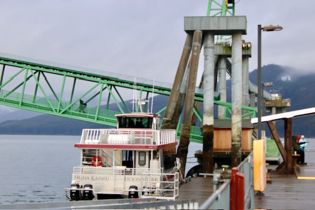 A white whale watching boat with red trim is at a dock.  A mint green walking bridge goes downhill in the background.  