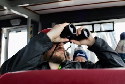 A man sits looking through binoculars. 