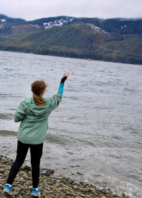 A young girl in a seagreen jacket throws a rock into the ocean at Icy Strait Point beach. 