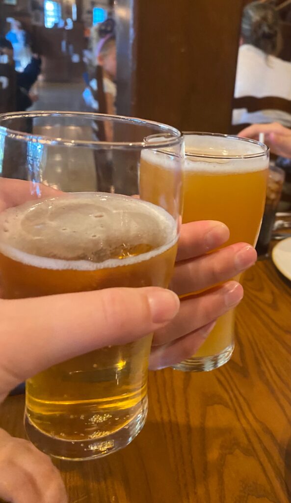 Two pilsner glasses  of light beer are being held to "cheers" .