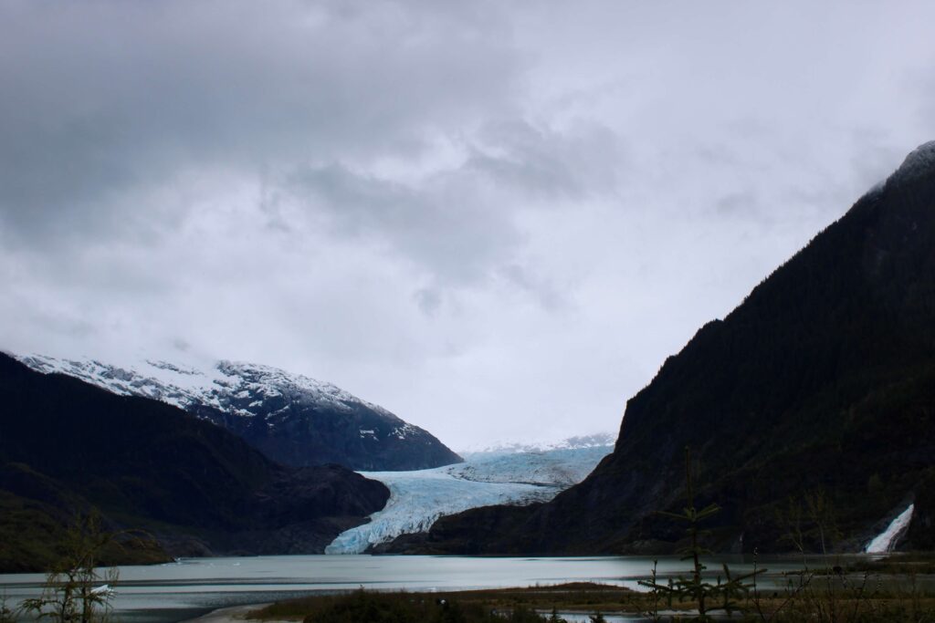 Mendenhall Glacier sits in the valley between two mountains.  A lake is in front of the glacier.  