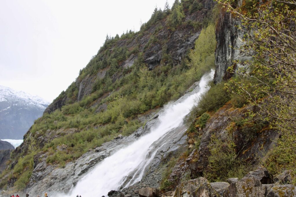 A waterfall runs down the side of a mountain that is covered in greenery. 