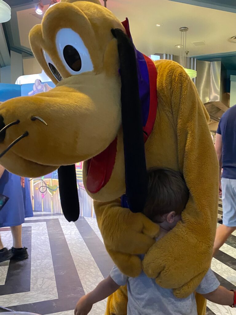 Walt Disney's Pluto hugs a child.  The child is almost completely hidden by Pluto's arms.  