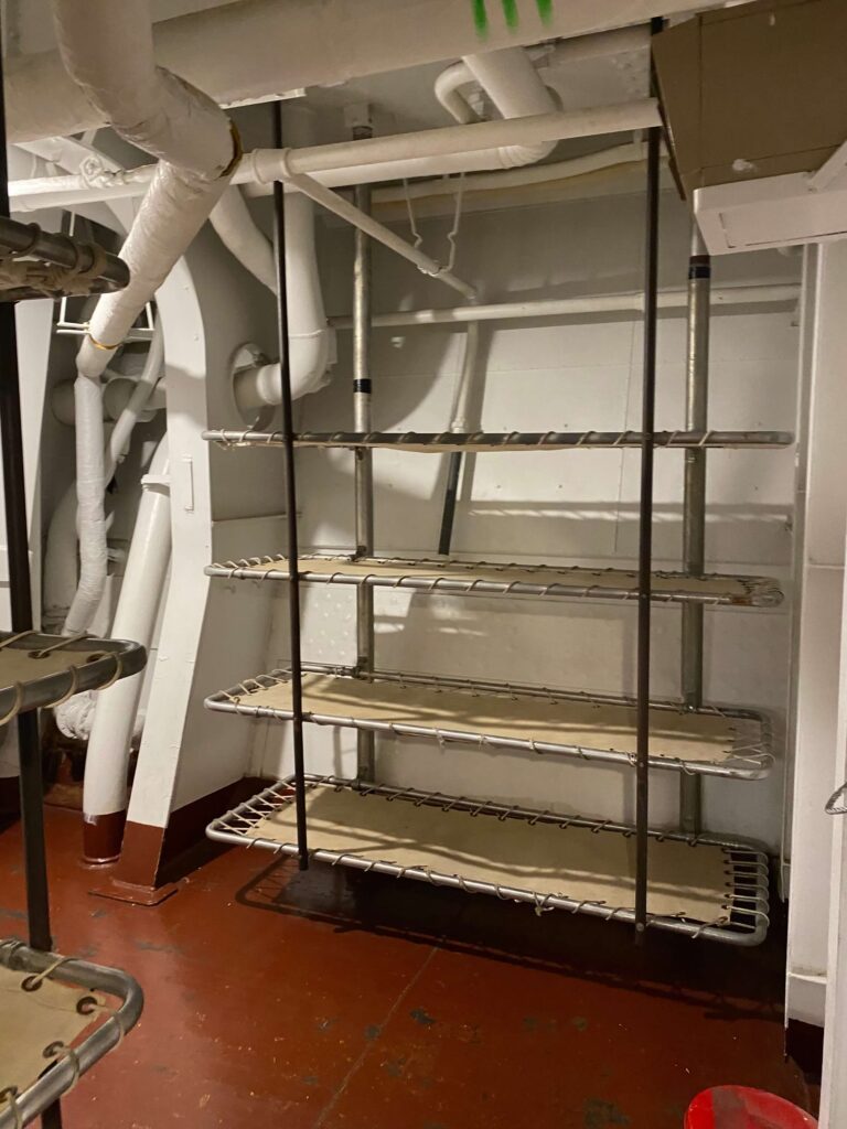 Cots are stacked five high as bunkbeds aboard a battleship. 