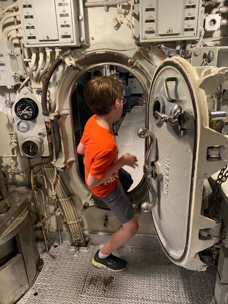 A child enters a submarine hatch. 