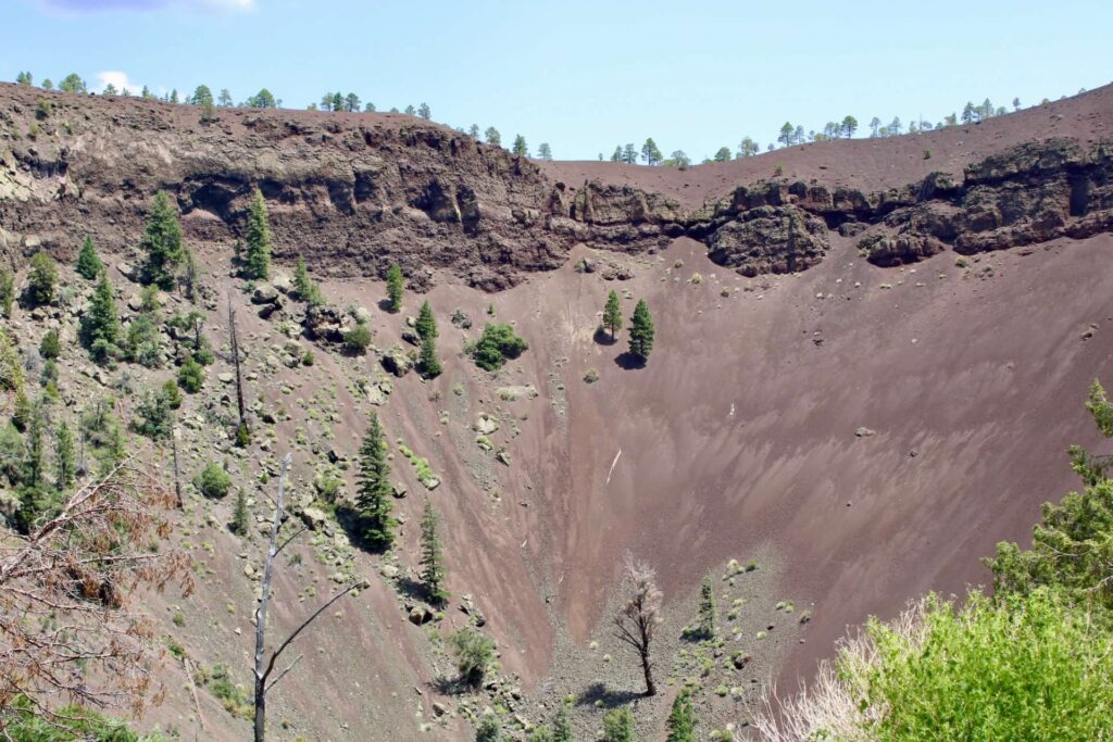 The cinder cone of Bandera Volcano is a depression in the mountain, all covered in dirt.  There are a few trees dotting the area. 