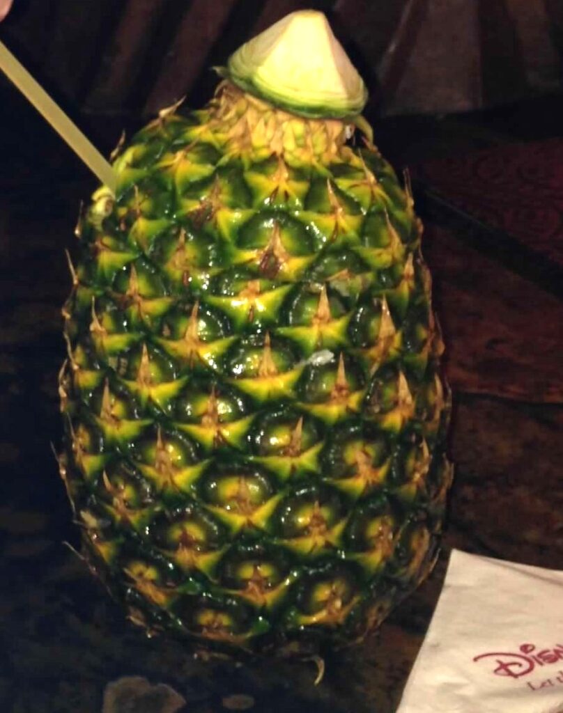 A pineapple has a straw sticking out of its side and the top cut off. 
