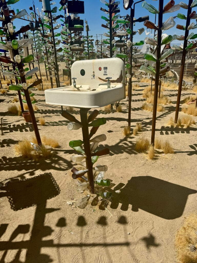 A bathroom sink from the 1950s or 1960s sits on top of a pole.  It is in the middle of Elmer's Bottle Tree Ranch in the Mohave Desert. 