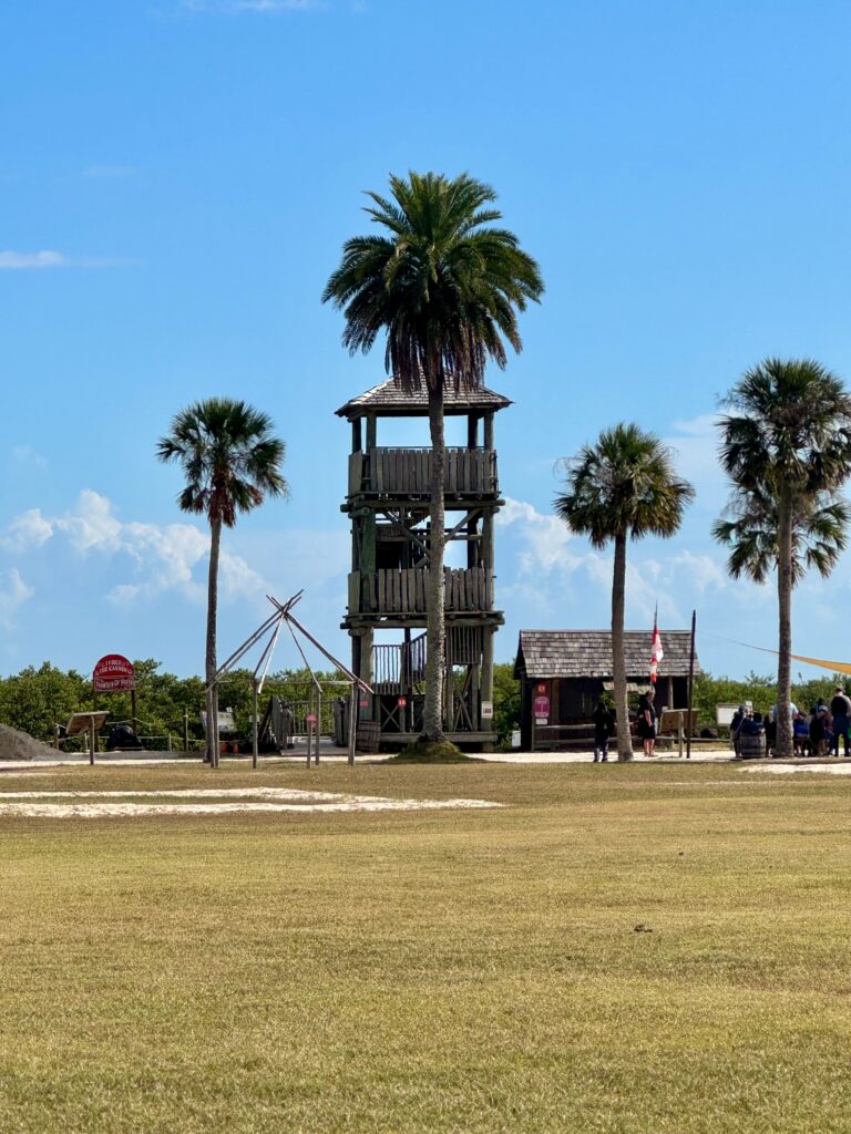 A watchtower is in the distance with palm trees dotting a blue sky.  