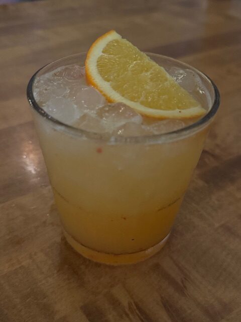 An orange drink in a clear glass with ice and an orange slice on top. 