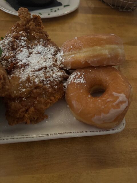 A plate of fried chicken and two glazed donuts are dusted with powdered sugar. 