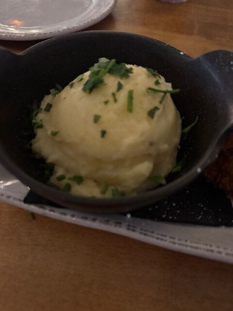 A smalls cast iron dish holds a scoop of mashed potatoes with chives on top of it.