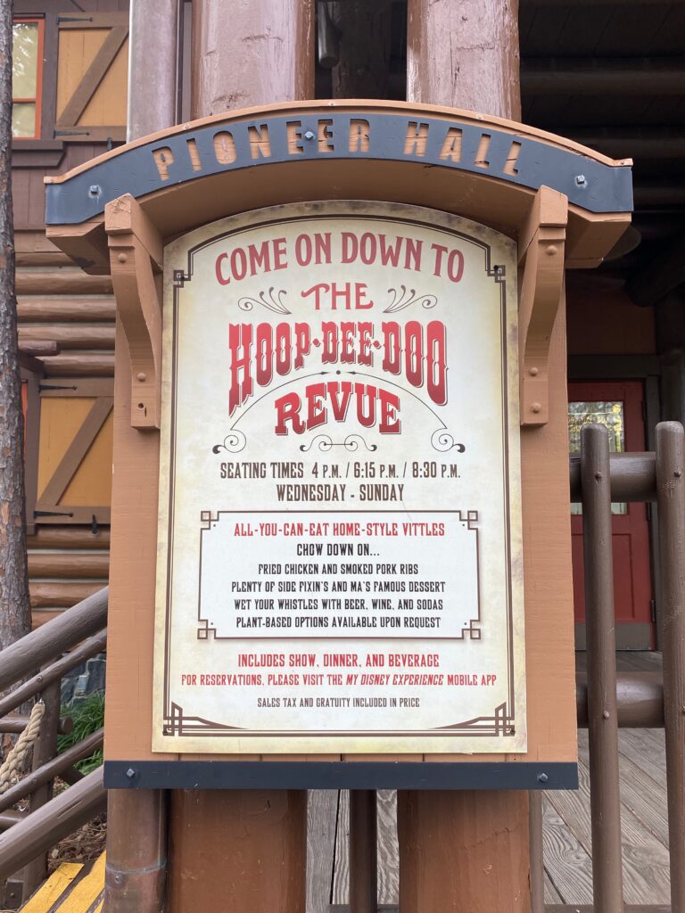 A sign with old time western font reads: Come on Down to the Hoop-Dee-Doo Revue.   Menu items are also written on it as well as show times. 