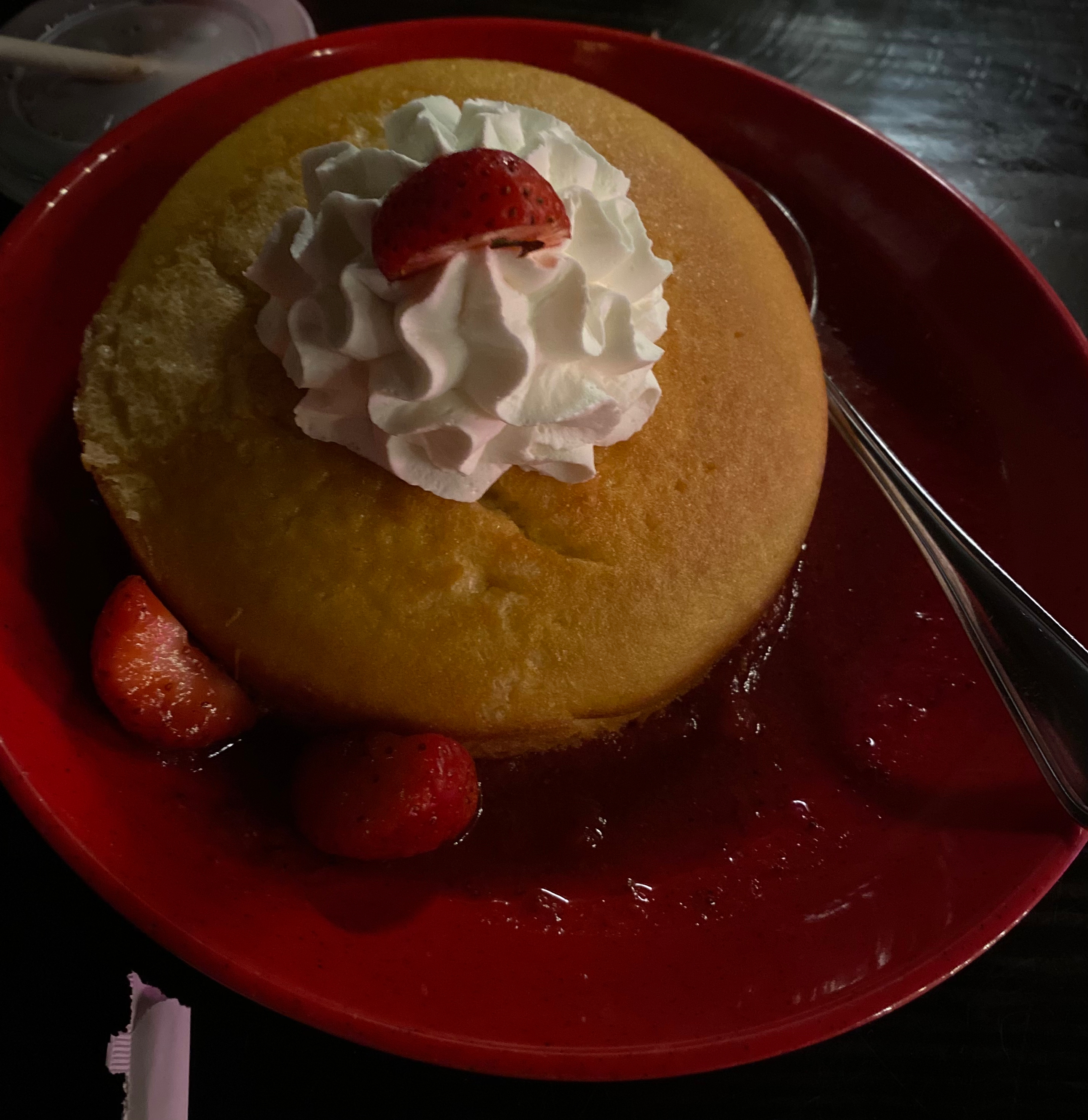 A round yellow cake sits on a red plate.  Whipped cream and strawberries sit atop of the cake and around the plate. 